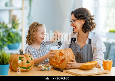 Glückliche Familie bereitet sich auf Halloween vor. Mutter und Kind schnitzen Kürbisse zu Hause. Stockfoto