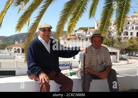 Zwei ältere spanische Männer sitzen an der Wand unter einer Palme, Frigiliana, Spanien. Stockfoto