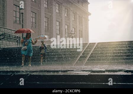 Verschwommene Silhouetten der Menschen beim Gehen auf einem Regen unter Regenschirmen. Regenwetter in der europäischen Stadt, Stockfoto