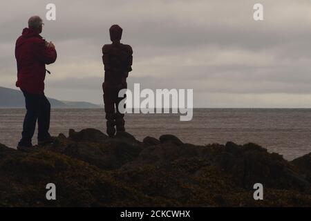 Anthony Gormleys Skulptur, GRIP und ein Mann 60+, der auf Felsen in Saddell Bay, Kintyre, Argyll, Schottland steht und zusammen über den Kilbrannan Sound blickt Stockfoto