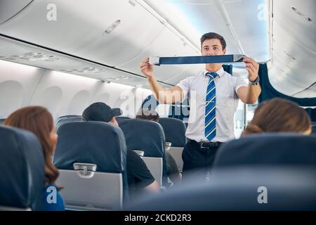 Nahaufnahme Porträt von jungen selbstbewussten Mann Flugbegleiter in Business Uniform zeigt, wie die Förderung der Beifahrersitzgurt Stockfoto