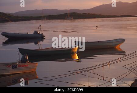 Abendsonne über Carsaig Bay, Tayvallich, Argyll, Schottland, mit vier kleinen Boote und Festmacherseilen im Untergrund, die sich im Wasser spiegeln Stockfoto