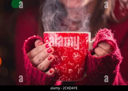 Detail der Frau Hände halten warm bei einer Tasse Tee mit Dampf. Blur Weihnachten Hintergrund. Weihnachten und Winter Konzept. Stockfoto