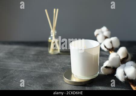 Hygge und Aromatherapie Konzept. Aroma Schilf Diffusor, Zweig aus Baumwolle und weiße Soja Kerze auf grauen Tisch zu Hause. Minimal Stil Zusammensetzung. Winter und Herbst Stimmung Stockfoto