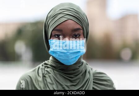 Porträt der schwarzen muslimischen Frau trägt blaue medizinische schützende Gesicht Maske im Freien Stockfoto