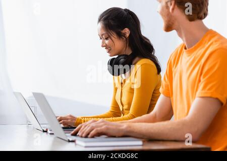 Selektive Fokus der Freiberufler mit Laptop in der Nähe asiatische Frau mit Kabellose Kopfhörer am Hals Stockfoto