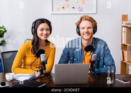 Junge Radiomoderatoren in kabellosen Kopfhörern, die die Kamera in der Nähe betrachten Mikrofone im Studio Stockfoto