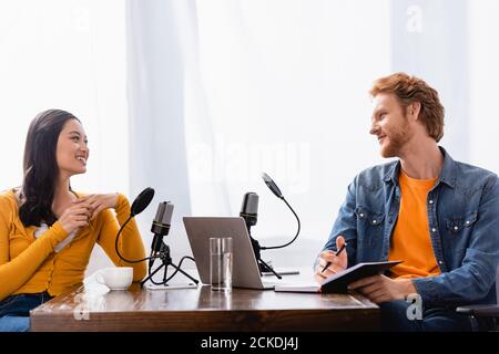 Rotschopf Sender hält Notebook und Stift während Interviews asiatische Frau Im Studio Stockfoto