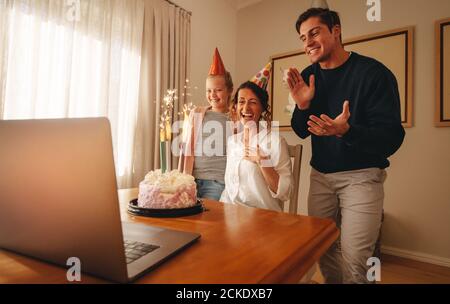 Frau feiert Geburtstag zu Hause mit Familie und Freunden auf Videoanruf. Familie feiert Mutter Geburtstag online. Stockfoto