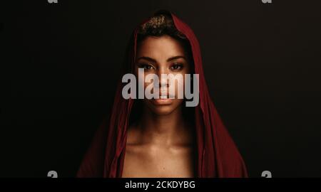 Porträt der afroamerikanischen Frau auf schwarzem Hintergrund. Frau trägt kastanienbraunen Stoff auf dem Kopf isoliert auf schwarzem Hintergrund. Stockfoto