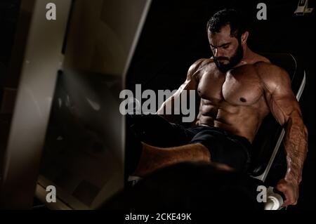 Schweres Training von bärtigen starken Mann in Fitnessgeräten Während des Trainings der Beinpresse Stockfoto