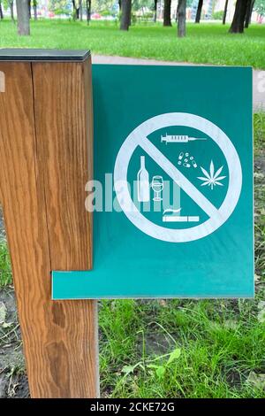 Schild, das Alkohol, Zigaretten, Drogen auf dem Hintergrund von grünem Gras im Park verbietet. Symbol auf Metallplatte. Stockfoto