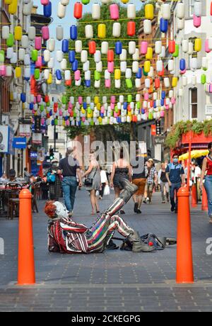 London, England, Großbritannien. Ein Clown (Straßenunterhalter) liegt auf dem Boden in der Wardour Street, Chinatown Stockfoto