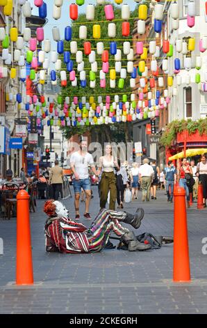 London, England, Großbritannien. Ein Clown (Straßenunterhalter) liegt auf dem Boden in der Wardour Street, Chinatown Stockfoto