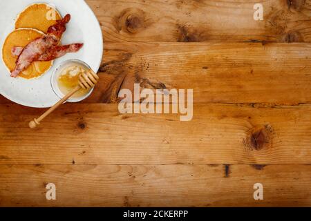 Ein Teller mit Speck und Pfannkuchen, beträufelt mit Honig auf einem rustikalen Holzhintergrund mit Platz für Kopie Stockfoto