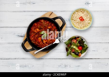 Ein traditionelles Blatigericht, gefüllt mit köstlichem balti-Hühnercurry, garniert mit einem Korrianderzweig, auf einem hölzernen Servierbrett, mit einer Beilage Stockfoto