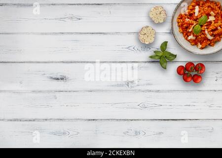 Eine Schüssel mit leckeren Tomatenpasta in einer rustikalen Schüssel, garniert mit einem Zweig Basilikum, mit Zutaten, auf einem weißen Holzhintergrund mit Platz für Kopie Stockfoto