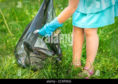 Kind sammelt Plastikmüll vom Gras und wirft Müll in den Müll Tasche im Park Stockfoto