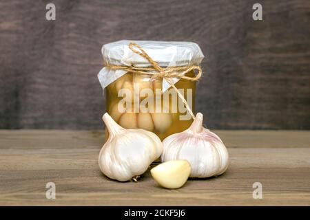 Marinierter Knoblauch im geschlossenen Glas und frisch auf Holz Tabelle gesunde fermentierte Lebensmittel hausgemachte Gurken Stockfoto