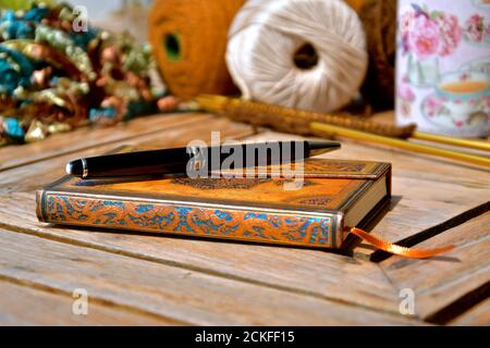 Konzept der Entspannung mit einem Leder gebunden Journal und Luxus Stift vor einem Hintergrund von verschiedenen Strickzubehör in einem Stillleben Komposition Stockfoto