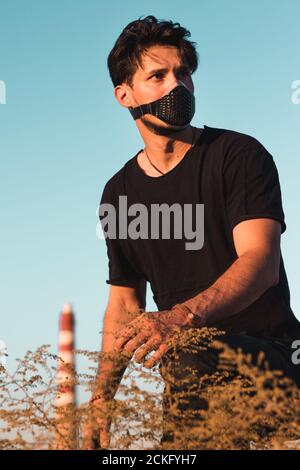 Ein physisch entfernter und sozial verbundener junger Mann in einem Schwarzes Outfit in einer Industriezone Stockfoto