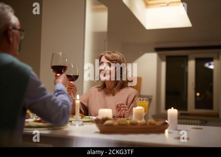 Seniorenpaar sitzt am Tisch und rösten mit Rot Wein beim Abendessen in der Küche Stockfoto
