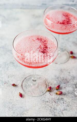 Rosafarbener Alkoholcocktail mit Limonade, Champagner oder Martini in einem Sektglas, mit Schaum und mit trockenen Rosenknospen verziert, Cocktail wie Daiquiri, Stockfoto