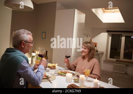 Ältere glückliche Paar hält Gläser mit Rotwein während des Abendessens In der Küche Stockfoto