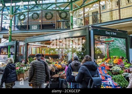 Menschen, die an einem Obst- und Gemüsemarkt im Londoner Borough Market, einem der größten und ältesten Lebensmittelmärkte Londons, vorbeigehen Stockfoto