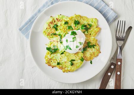 Gemüsezucchini-Pfannkuchen mit pochiertem Ei auf weißem Teller. Draufsicht Stockfoto