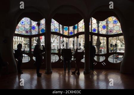 Besucher beobachten das große Buntglasfenster im zentralen Salon des edlen Bodens in der Casa Batlló in Barcelona, Katalonien, Spanien. Das Herrenhaus, das vom katalanischen modernistischen Architekten Antoni Gaudí für die Familie Batlló als Einnahmehaus sowie als private Familienresidenz entworfen wurde, wurde zwischen 1904 und 1906 erbaut. Stockfoto