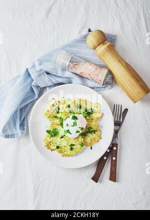 Gemüsezucchini-Pfannkuchen mit pochiertem Ei auf weißem Teller. Draufsicht Stockfoto