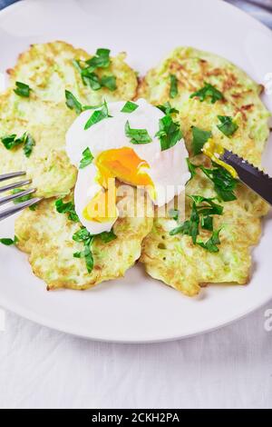 Gemüsezucchini-Pfannkuchen mit pochiertem Ei auf weißem Teller Stockfoto