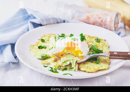 Gemüsezucchini-Pfannkuchen mit pochiertem Ei auf weißem Teller Stockfoto