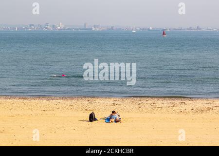 Eine Frau, die alleine an einem goldenen Sandstrand, Ryde, Isle of Wight, sonnenbaden geht Stockfoto