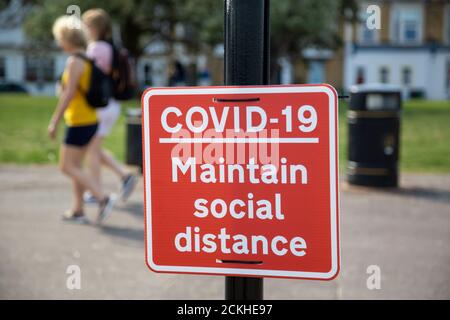 Menschen, die an einem Schild auf einem Laternenpfahl vorbeigehen, auf dem steht Covid-19 Beibehalten Sie soziale Distanz Stockfoto