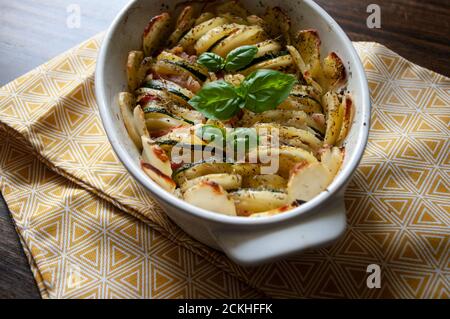 Herzhafte Kartoffelgratin Speck und Zucchini, frisch aus dem Ofen auf einer gelben Tischdecke serviert. Stockfoto