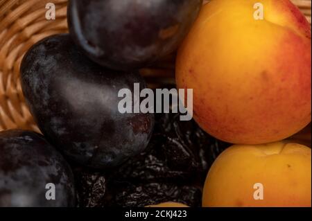 Reife Aprikosen, saftige schwarze Pflaumen und getrocknete Pflaumen in einem Weidenkorb. Nahaufnahme. Herbsternte Stockfoto