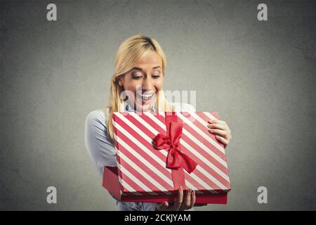 Nahaufnahme Porträt junge glücklich aufgeregt Frau Eröffnung rote Geschenkbox, sehr zufrieden und dankbar mit dem, was sie isoliert auf grauen Wand Hintergrund erhalten. Po Stockfoto