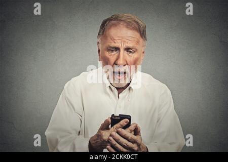 Nahaufnahme Porträt, lustig älteren Mann, schockiert mit weit offenen Mund überrascht, von dem, was er sieht auf seinem Handy isoliert auf grauen Wand Hintergrund Stockfoto