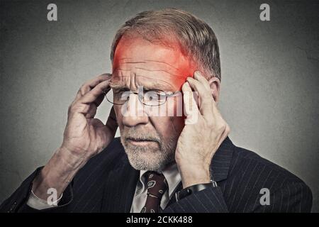 Nahaufnahme Kopfschuss Senior Mann leiden unter Kopfschmerzen Hände auf Kopf mit rot gefärbten entzündeten Bereichen Blick nach unten isoliert auf grauen Wand Hintergrund. Mensch Stockfoto