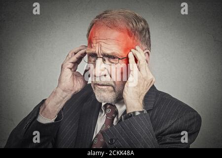 Nahaufnahme Kopfschuss Senior Mann leiden unter Kopfschmerzen Hände auf Kopf mit rot gefärbten entzündeten Bereichen Blick nach unten isoliert auf grauen Wand Hintergrund. Mensch Stockfoto