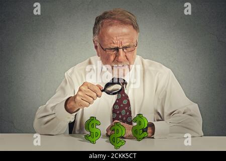 Penny Pincher. Senior skeptisch Geschäftsmann Blick durch Lupe auf Dollar-Symbol isoliert grauen Hintergrund. Wirtschaft Finanzvermögen Stockfoto