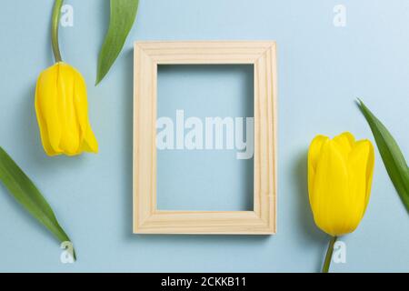 Hölzerner Fotorahmen mit gelben Tulpenblüten auf blauem Hintergrund. Draufsicht, Kopierraum Stockfoto