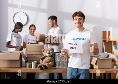 Selektive Fokussierung der freiwilligen Karte mit Dankesbeschriftung Und zeigt den Daumen nach oben in Charity-Center Stockfoto