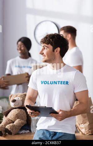 Selektiver Fokus von Freiwilligen halten Zwischenablage und Stift in der Nähe weich Spielzeug- und Papiertüte im Charity Center Stockfoto