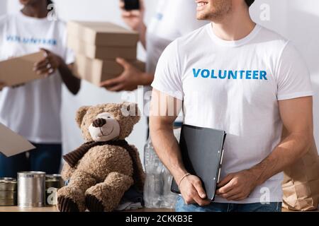 Beschnittene Ansicht der Freiwilligen hält Zwischenablage in der Nähe von Dosen und Weiches Spielzeug im Charity Center Stockfoto