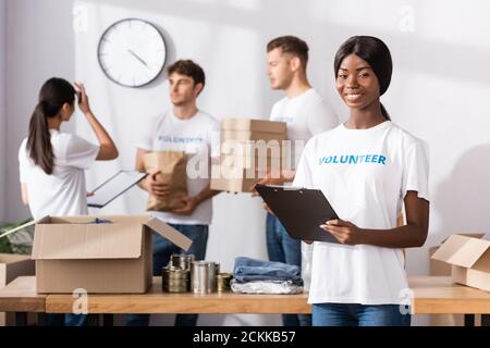 Selektiver Fokus der afroamerikanischen Frau im T-Shirt mit Freiwilliger Schriftzug hält Zwischenablage in Charity-Center Stockfoto