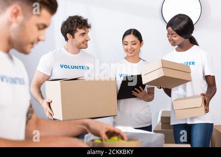 Selektiver Fokus von multiethnischen Freiwilligen halten Zwischenablage und Boxen in Wohltätigkeitszentrum Stockfoto