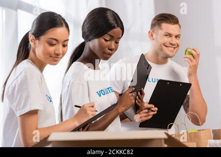 Selektiver Fokus der afroamerikanischen Freiwilligen hält Zwischenablage in der Nähe von Menschen Und Pakete in Charity Center Stockfoto